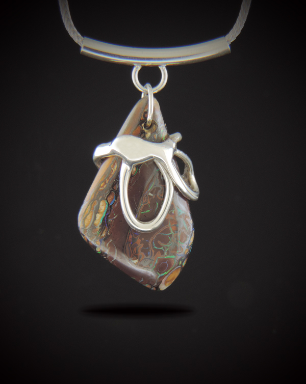 Alt Text: A vertical Australian Boulder Opal pendant with natural brown matrix and flashes of green and blue, encased in a custom-cast sterling silver wrap. The pendant hangs from a curved sterling silver tube bail on a woven foxtail chain.