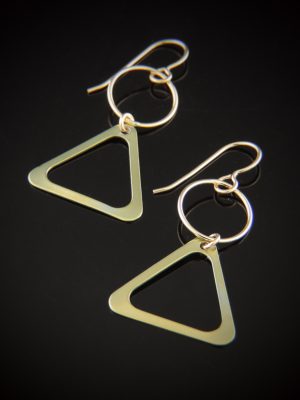 A pair of Milk & Honey earrings featuring large, thin gold-colored titanium triangles hanging from gold-filled circular links and earwires, displayed on a black background