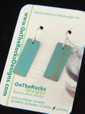 Crisp, contemporary titanium bar earrings featuring sleek rectangular drops in a soft aqua tone with subtle gold accents. Suspended from gold-filled fishhook ear wires, these minimalist geometric earrings offer a clean, modern silhouette with elegant movement. Approx. 1 3/8" long and 3/8" wide.