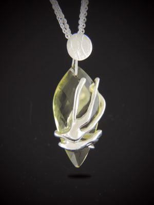 A faceted lemon quartz teardrop pendant wrapped in an organic cast sterling silver setting, suspended from a silver disk on a three-strand silver chain against a dark background.