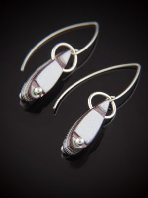 Pair of teardrop-shaped Fordite earrings with shimmery silver and red paint layers. The stones are suspended by sterling silver rings and feature a small silver bead at the bottom, hanging from long V-shaped sterling silver ear wires against a black reflective background.