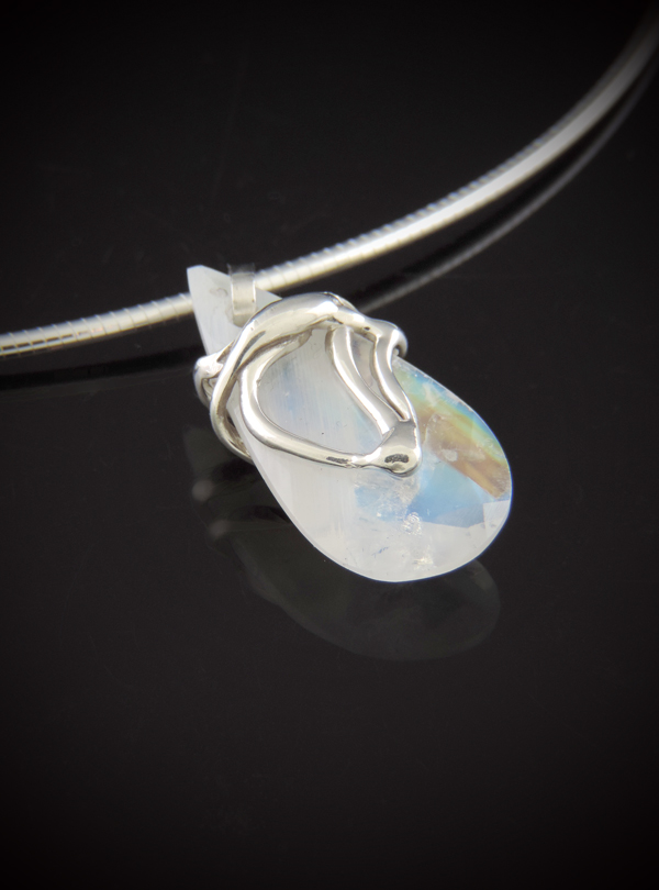 Perspective view of a rainbow moonstone necklace showing the iridescent blue flash of the stone and the organic, sculptural sterling silver setting.