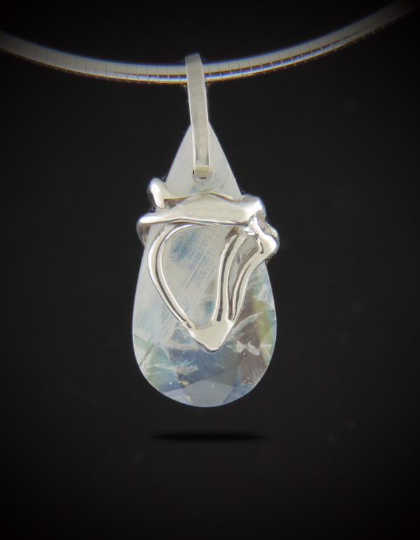 A teardrop-shaped rainbow moonstone pendant with a unique, hand-cast sterling silver swirl design hanging from a silver omega chain against a black background.