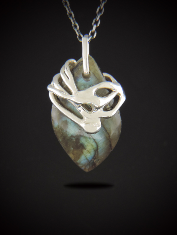 A teardrop-shaped Labradorite pendant with iridescent blue and green flashes, held by a contemporary, swirling sterling silver cast setting. The pendant hangs from a dark, shimmering diamond-cut chain against a black background.