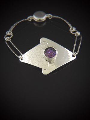A geometric sterling silver bracelet on a black surface, showcasing overlapping textured triangles centered with a sparkling, round purple 10mm titanium druzy, connected to a dark rhodium-plated link chain with a round magnetic clasp.