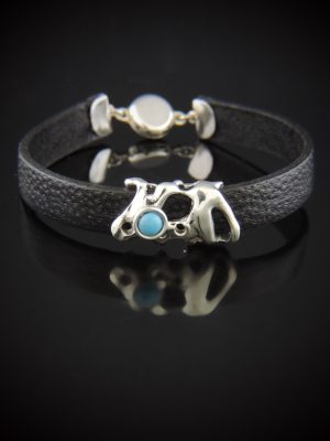 Bar Bandit unisex leather bracelet featuring a textured 10mm black leather band, a central organic-shaped cast sterling silver bar bead set with a small round blue turquoise cabochon, and a smooth silver magnetic twist clasp in the background on a black reflective surface.