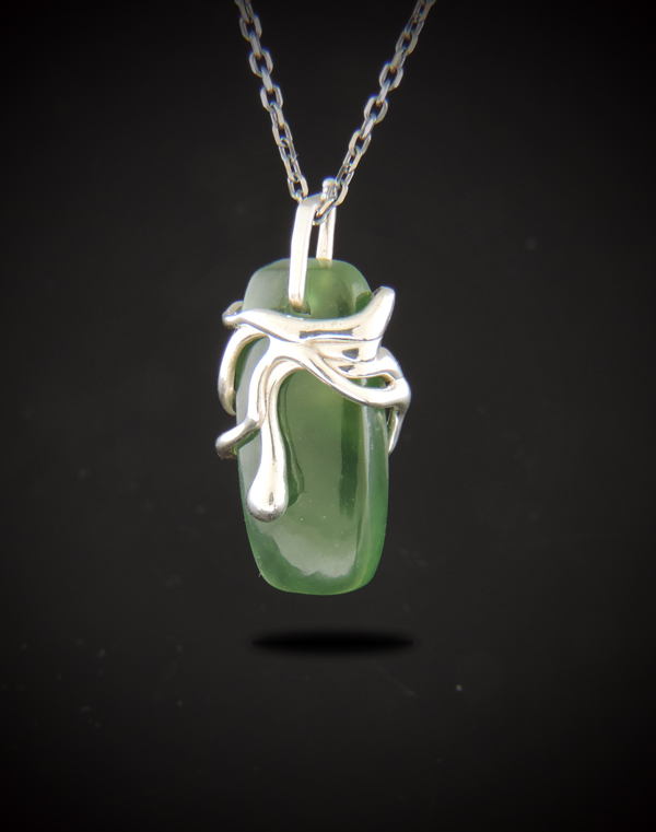 One-of-a-kind Lucky Charm pendant featuring a smooth green Canadian jade gemstone hugged by organic fluid-style cast sterling silver, suspended on a dark ruthenium-plated cable chain against a dark background.